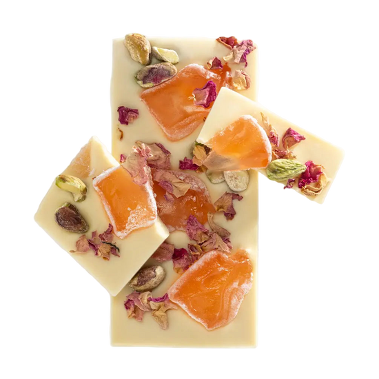 Three pieces of white chocolate with orange slices, dried fruits, and flowers on a white background