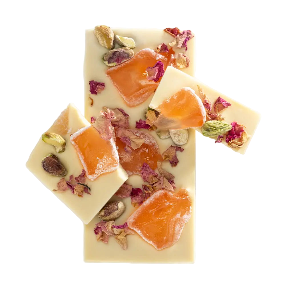 Three pieces of white chocolate with orange slices, dried fruits, and flowers on a white background