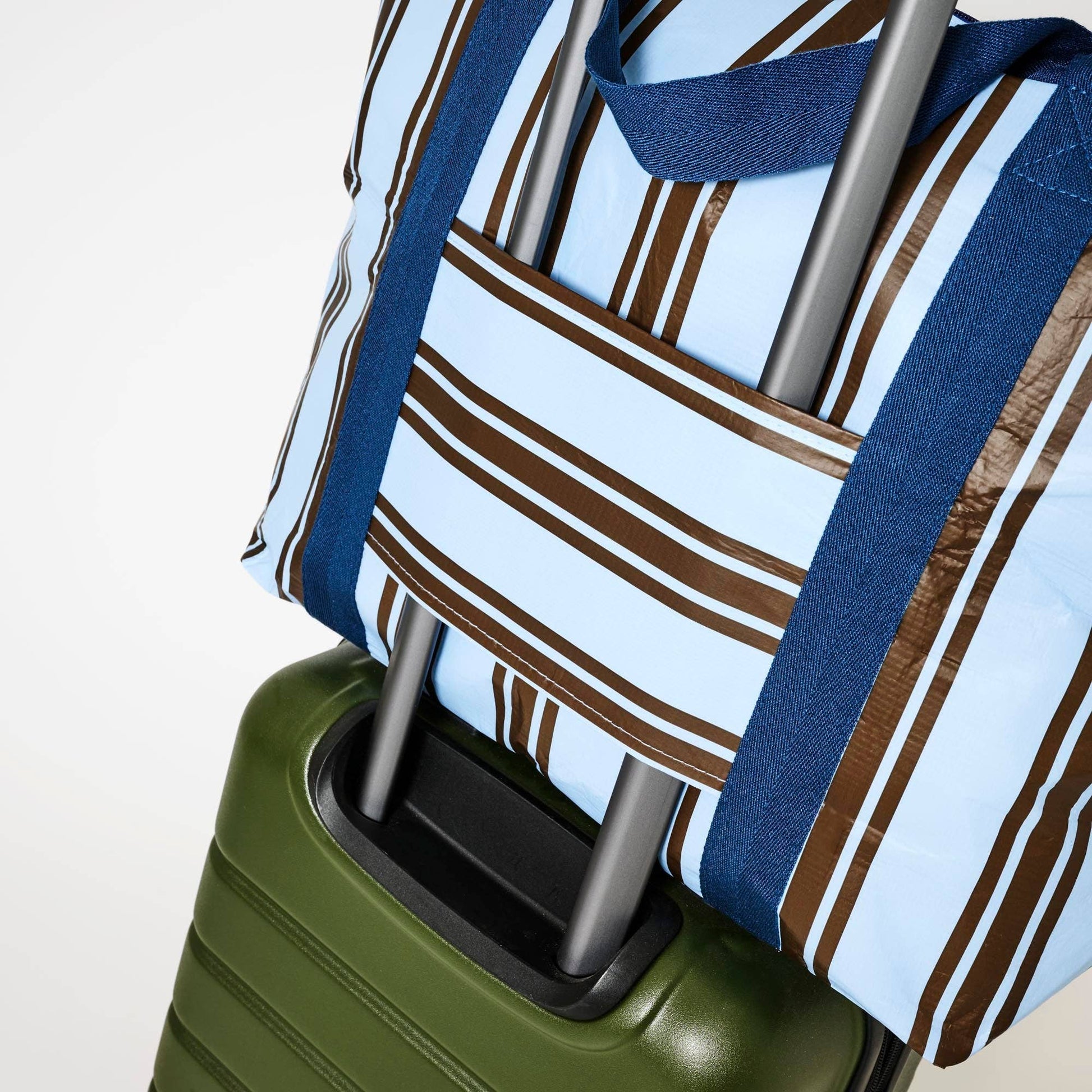 Green suitcase with a Zip Medium Tote  Oxford Stripe on top against a light background