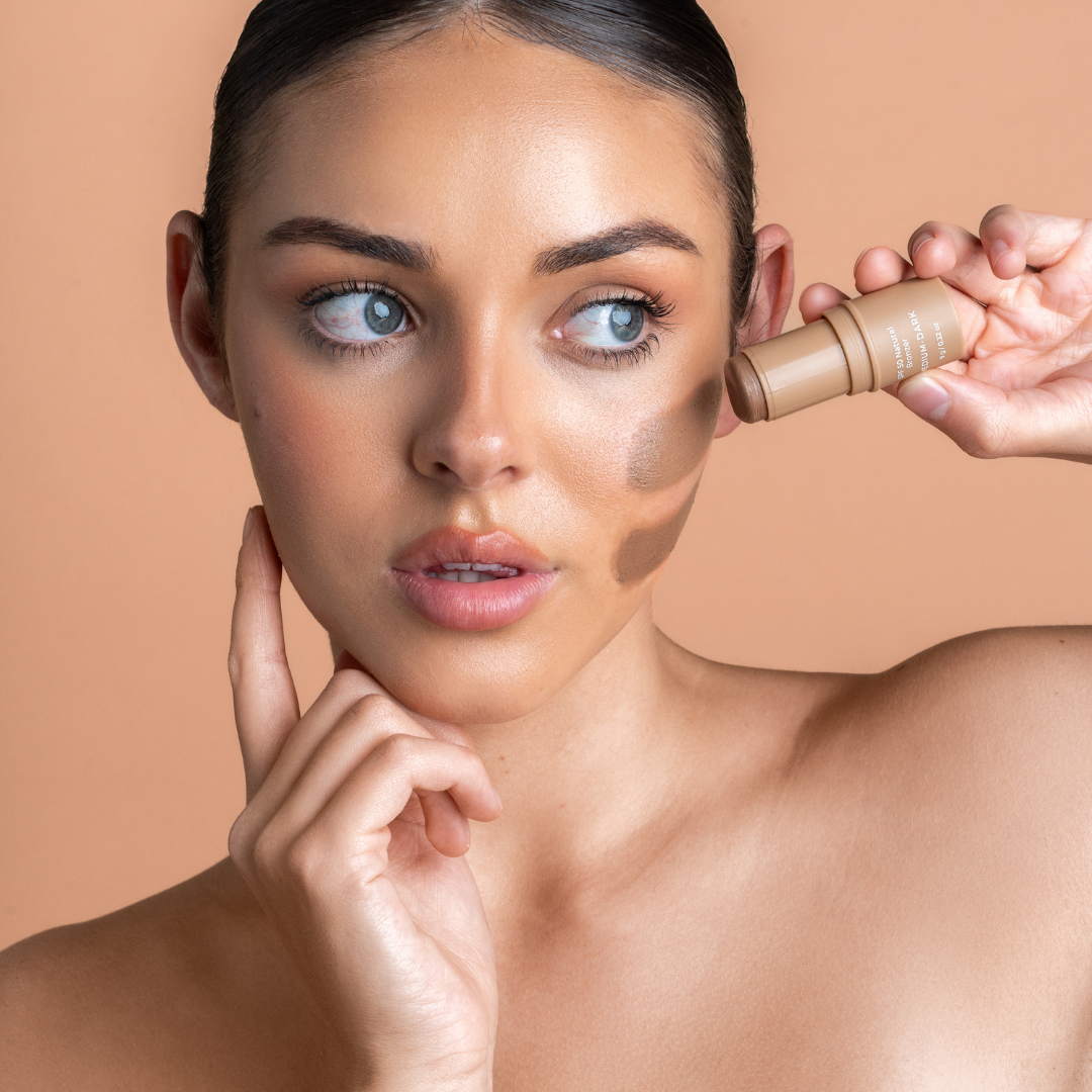Woman applying bronzer to her face with a sticker on a beige background
