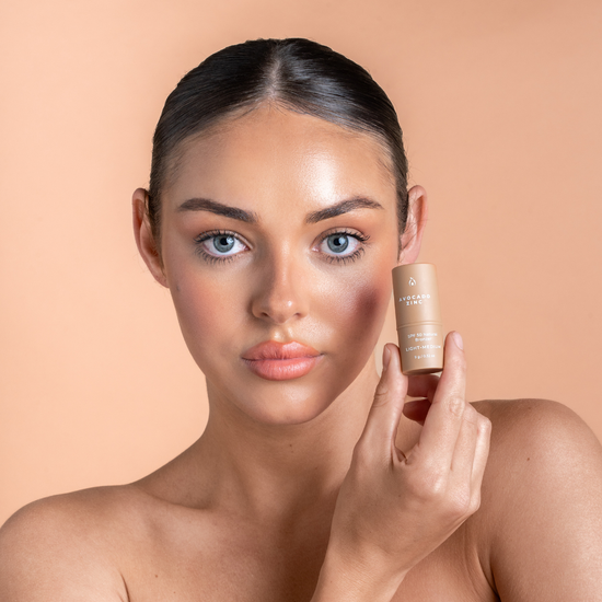 Woman holding a skincare bronzer product against a beige background