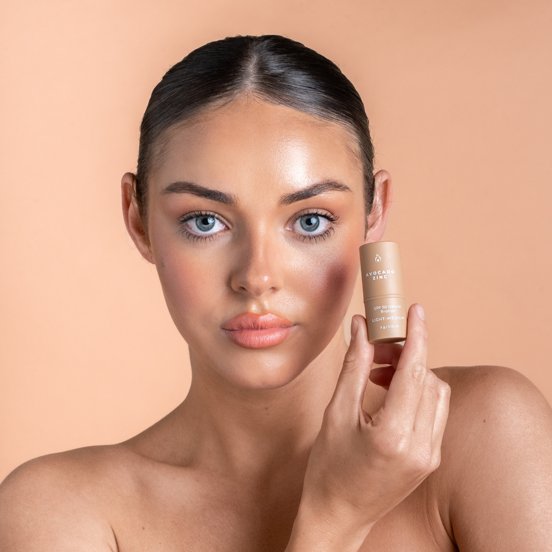 Woman holding a skincare bronzer product against a beige background