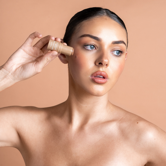 Woman applying bronzer makeup with a compact powder on a beige background