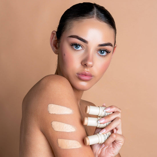 Woman holding avozinc products with swatches on her arm against a beige background