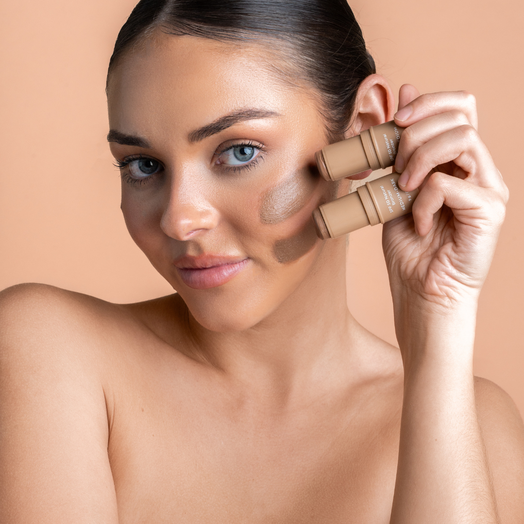 Woman applying contour makeup with a avozinc bronzer stick on a beige background