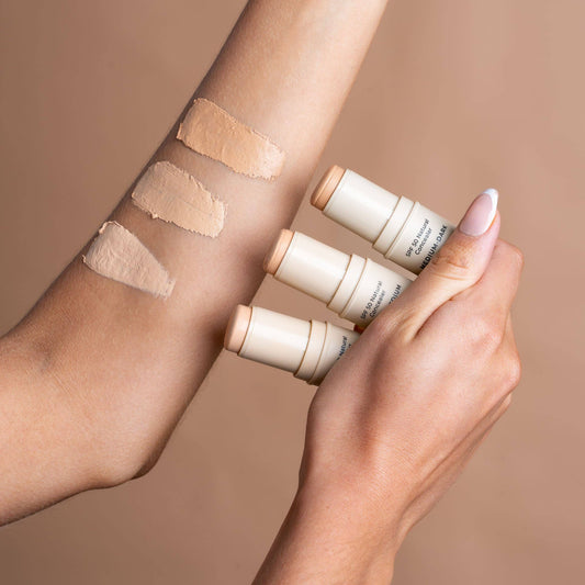 Hand holding avo zinc concealer products with swatches on a arm against a neutral background