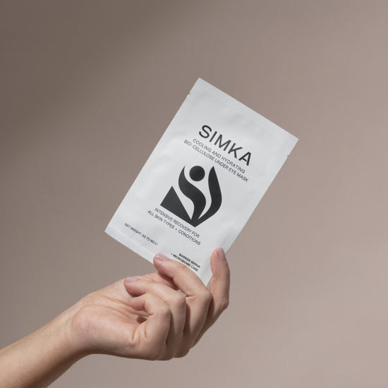 Hand holding a SIMKA product package against a beige background
