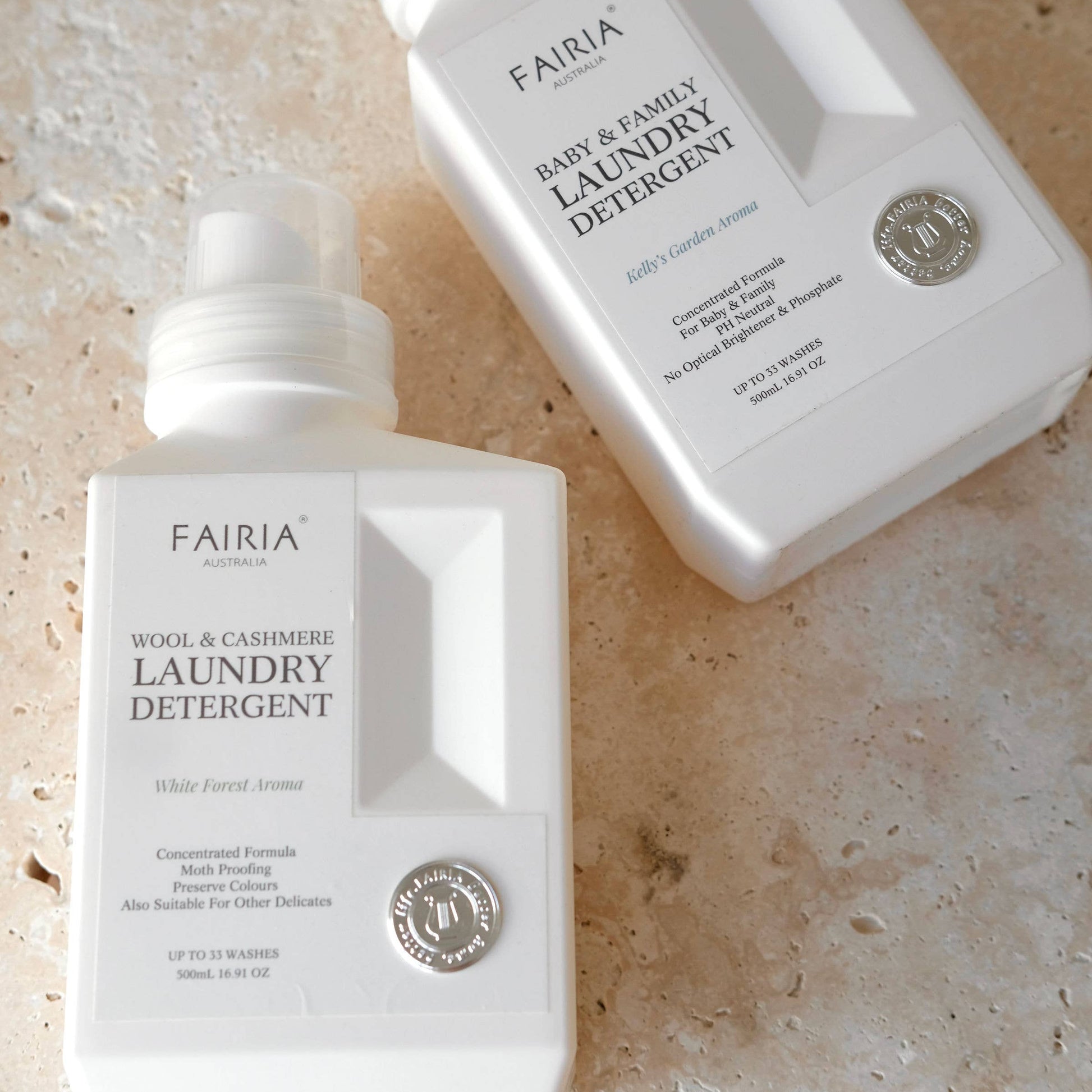 Two bottles of Fairia laundry detergents one baby & family and another wool & cashmere on a marble textured surface.
