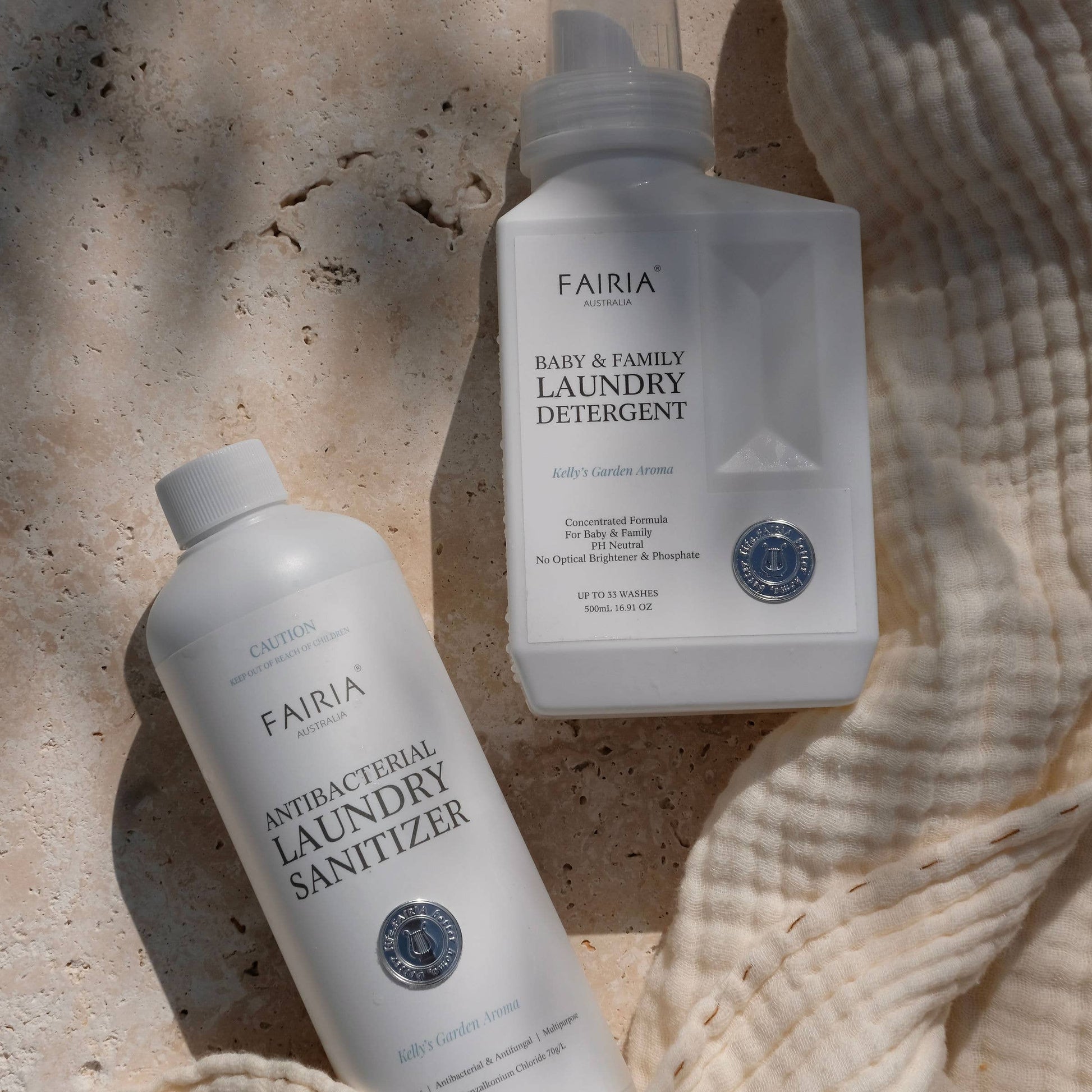 Two bottles of Fairia laundry detergent one baby & family laundry detergent another being the antibacterial laundry sanitizer products on a marble textured surface and a cotton beige blanket 