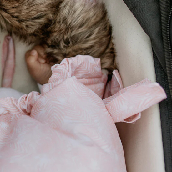 Close-up of a pink baby footmuff pram liner with fur hood and baby hand