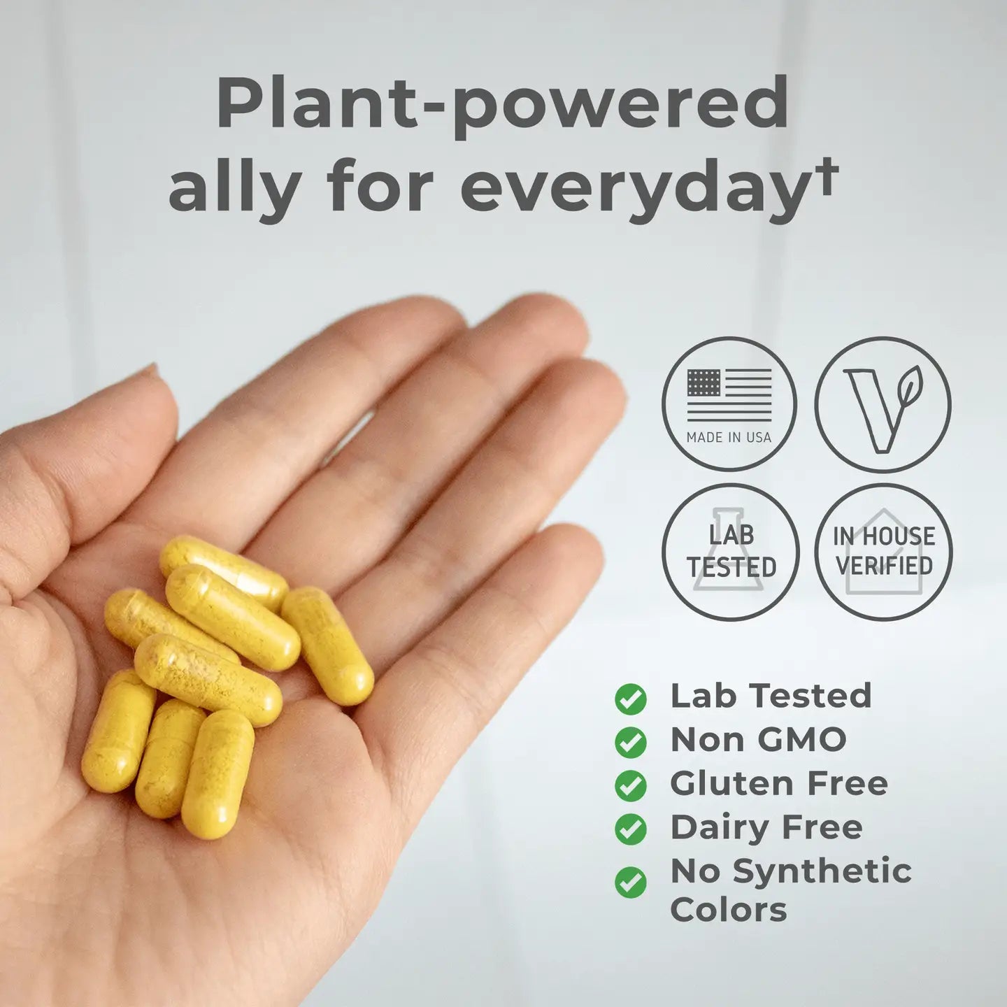 Hand holding yellow capsules with product features on a light gray background. Plant powered ally for everyday. Lab tested. Non GMO. Gluten free. Dairy free. No synthetic colors. 