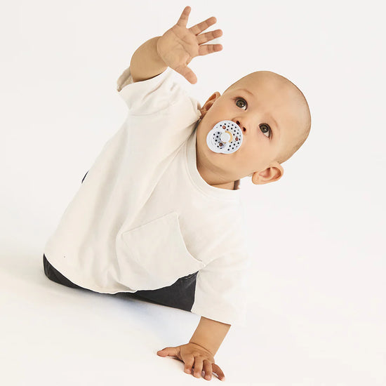 Baby with blue bibs polka dot dummy wearing a white outfit with a black bottom section on a light gray background