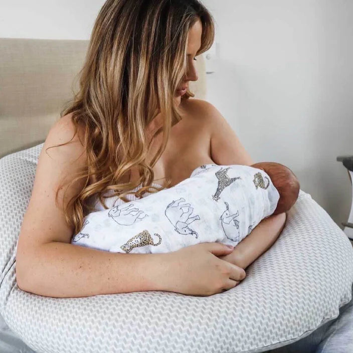 Woman holding a baby wrapped in a blanket on a a body pillow surface