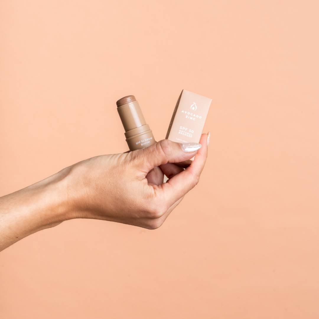 Hand holding a bronzer cosmetic bottle and its packaging against a beige background