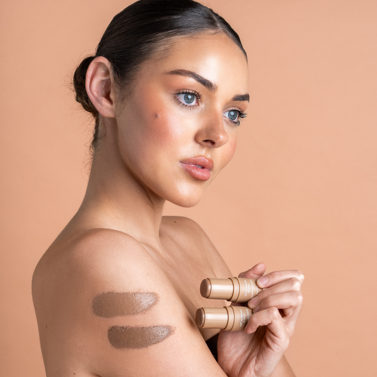 Woman holding makeup bronzer products against a beige background