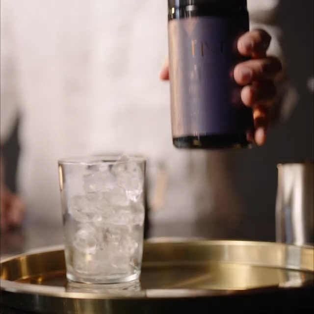 Person holding a bottle over a glass with ice on a tray