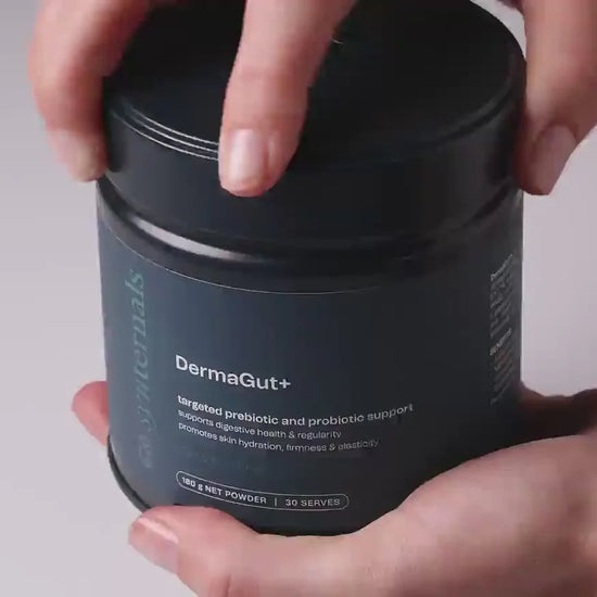 Person holding a navy container labeled 'DermaGut+' against a neutral background