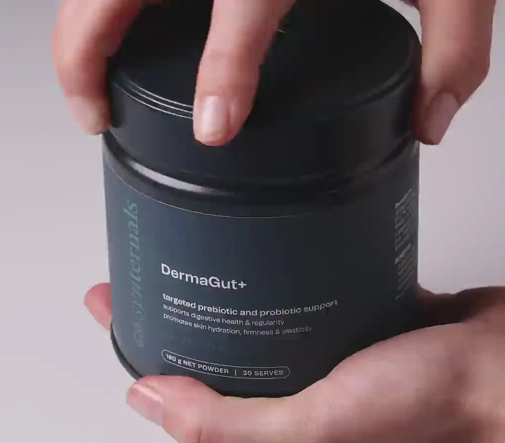 Person holding a navy container labeled 'DermaGut+' against a neutral background