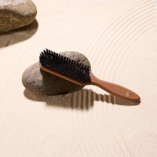 Wooden boar bristle hairbrush on a stone with sand background