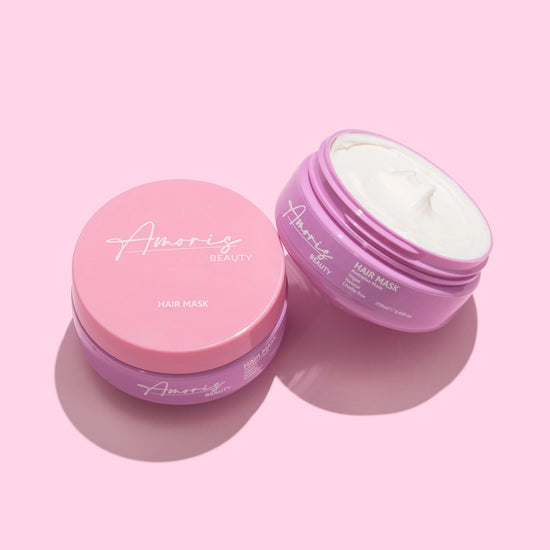 Two amoris hair mask containers with pink and purple lids on a pink background