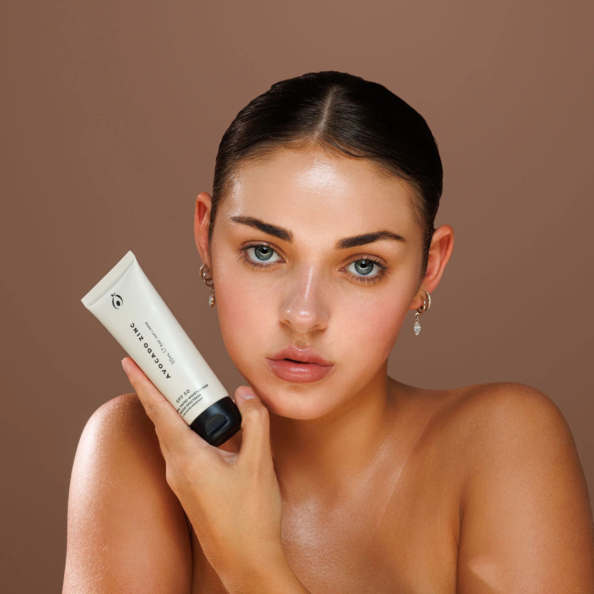Light avo zinc spf 50 Woman holding a skincare product against a brown background