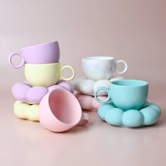 Colorful ceramic cups and saucers with unique handles on a pink background