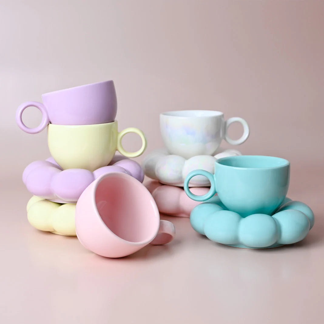 Colorful ceramic cups and saucers with unique handles on a pink background
