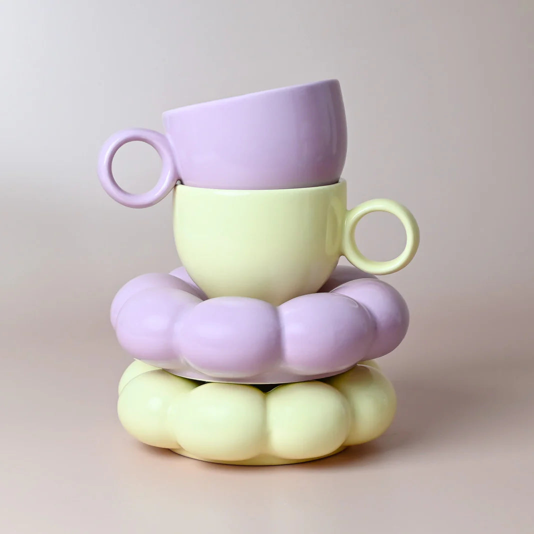 Stack of pastel-colored yellow and purple cups on a matching saucer against a neutral background