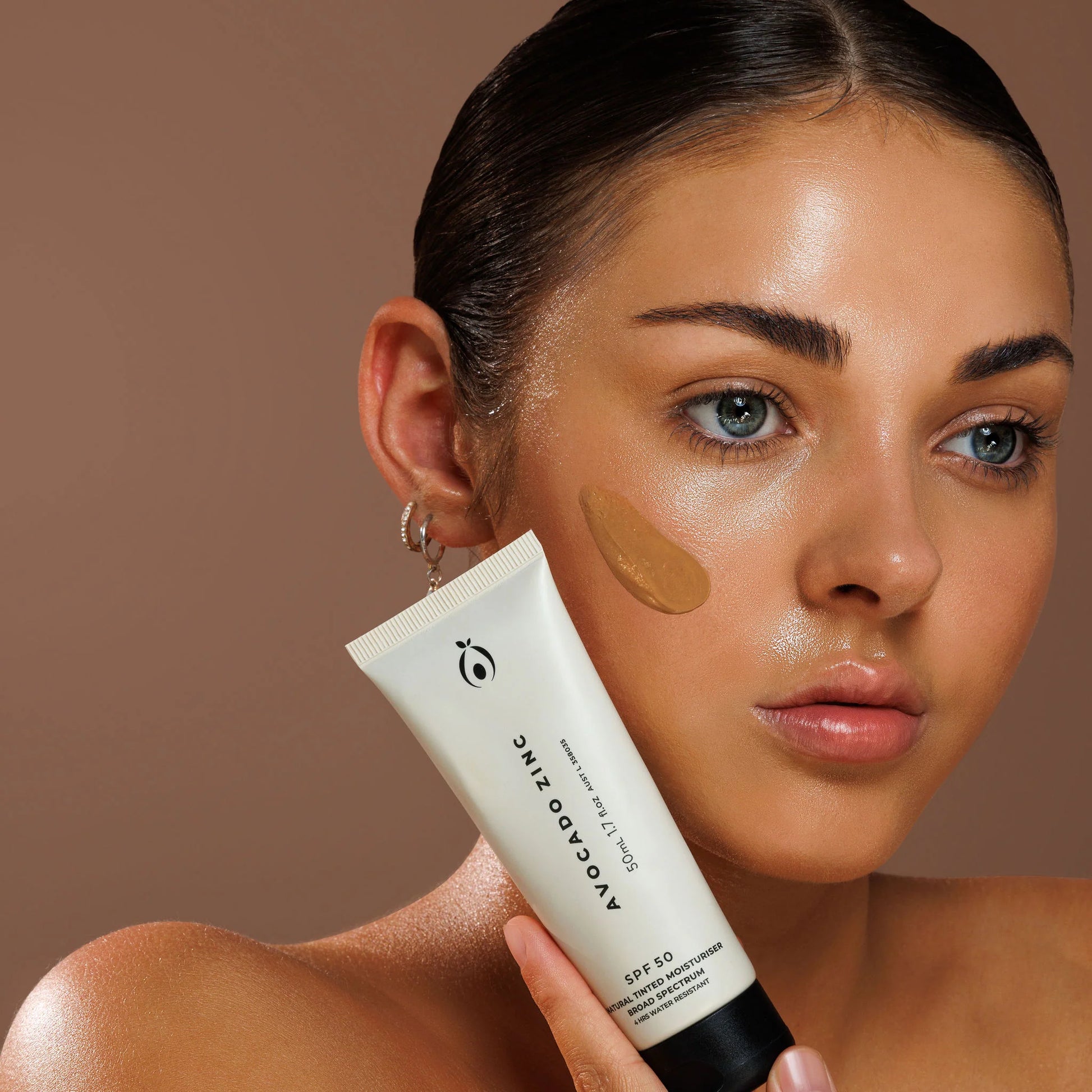 Woman holding a tube of tinted moisturiser product with a brown background