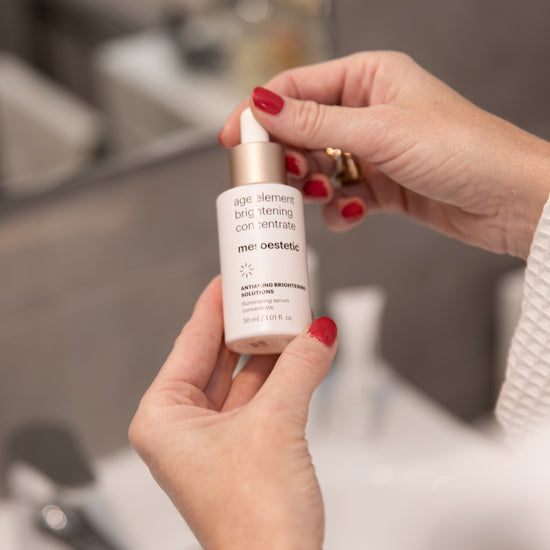 Person holding a brightening
age element brightening concentrate skincare product with a blurred background