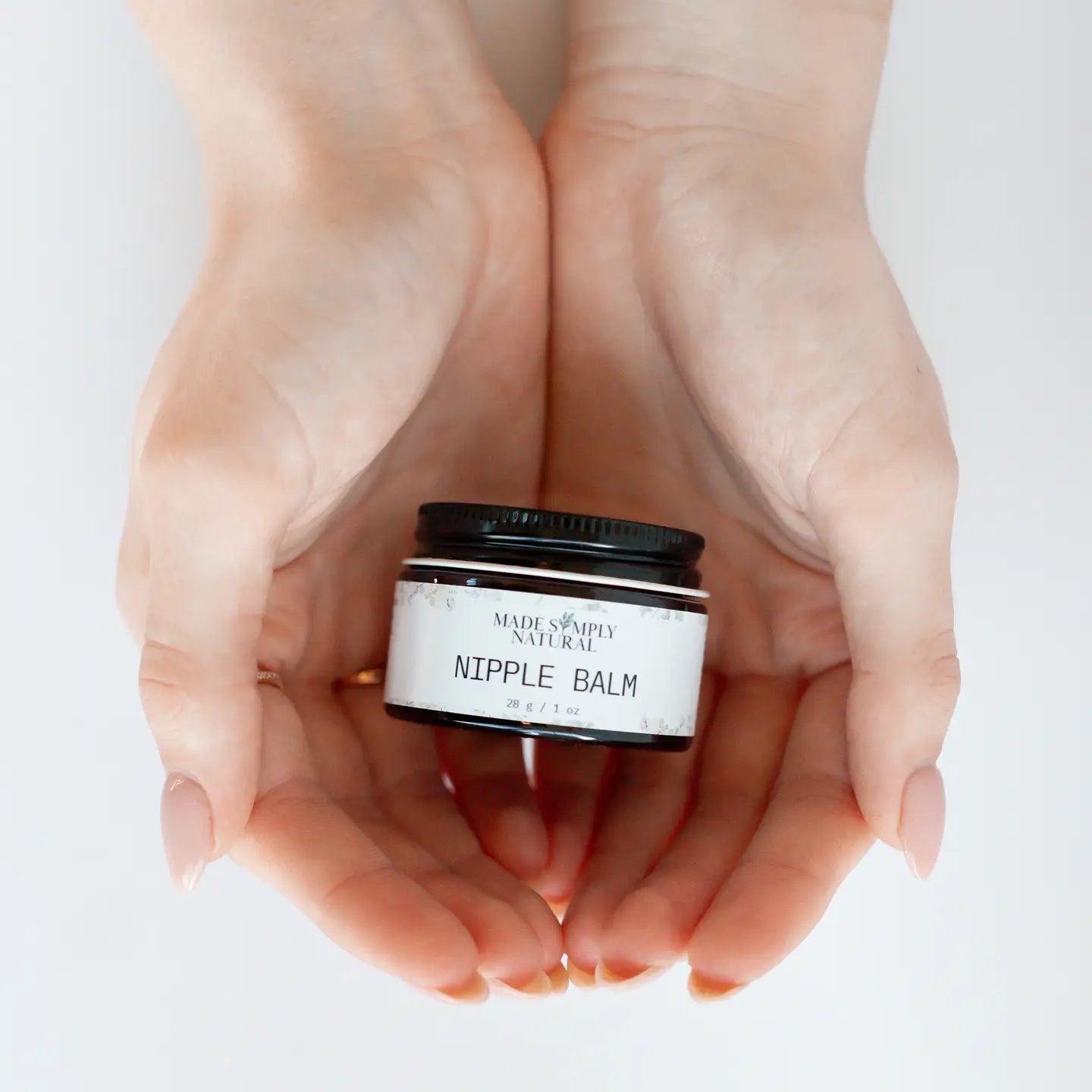Hands holding a jar of 'Nipple Balm' with a white label on a light background made simply natural