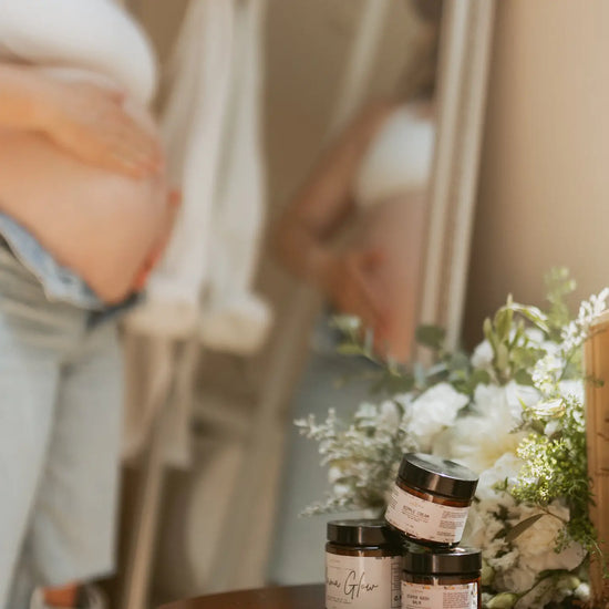Person holding baby belly with jars of nipple balm and flowers in the foreground