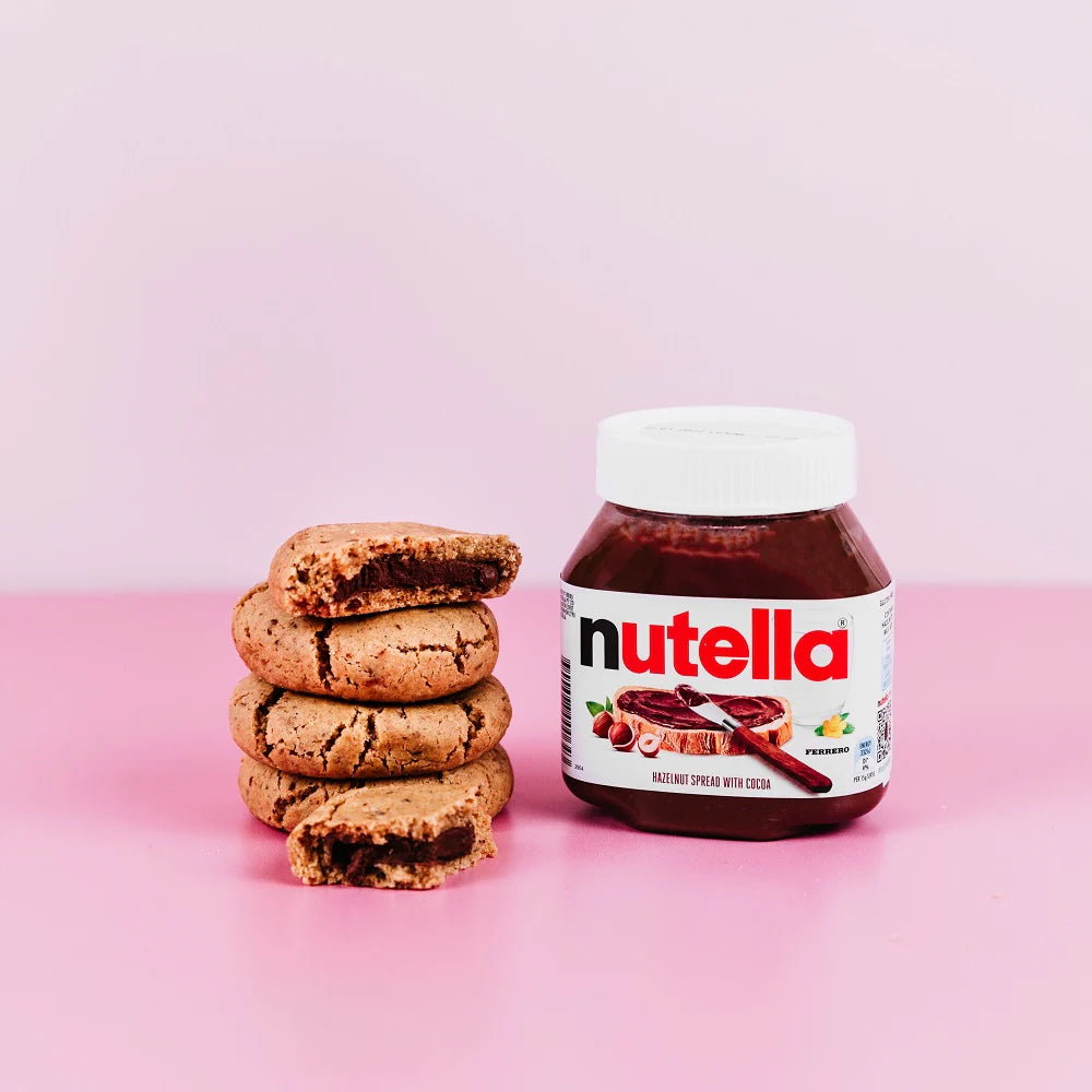 Jar of Nutella next to a stack of nutella lactation cookies on a pink background