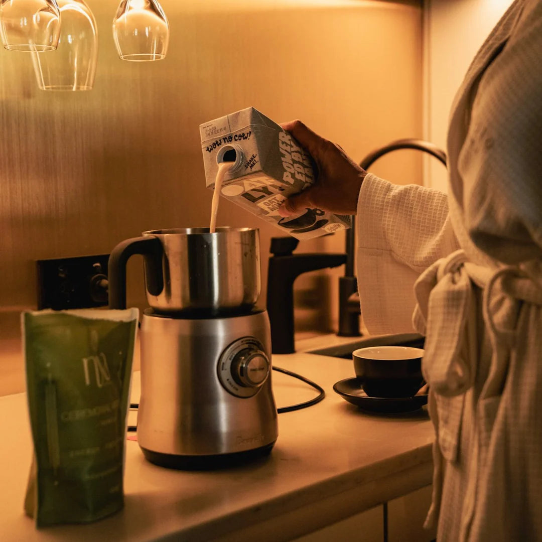 Person preparing matcha using a milk maker on a kitchen counter.