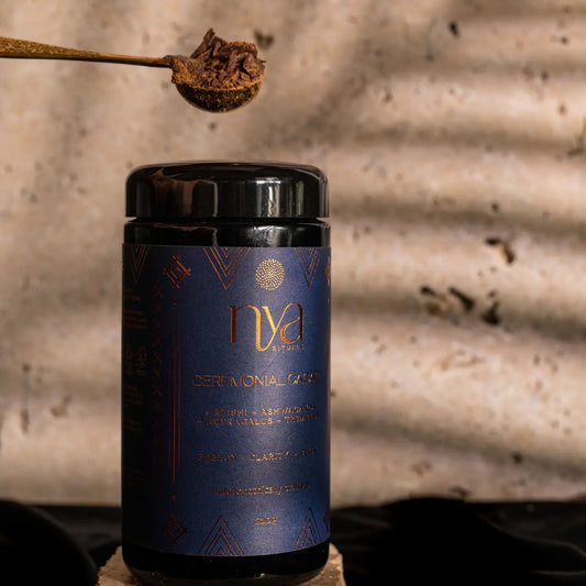 Container of ceremonial grade cacao with a spoonful of ground cacao above it on a rustic background.