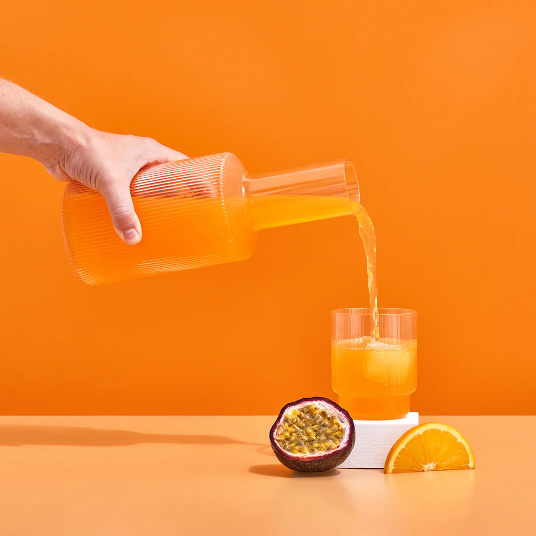 passion fruit and orange hydramama being poured into glass with passionfruit and orange sitting