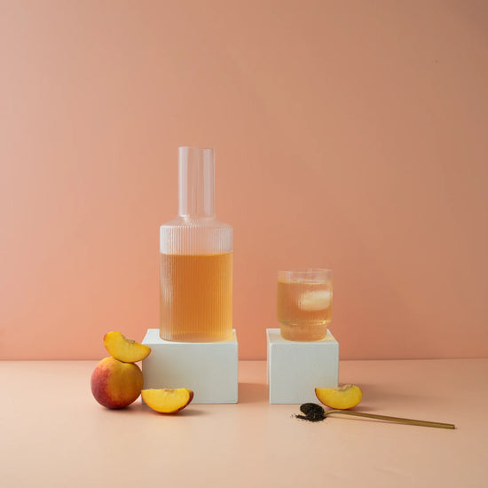 peach iced tea hydramama being poured into glass with peachs sitting