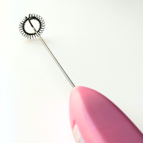 Pink handheld tool with a metal electric whisk on a white background