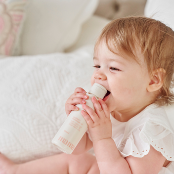 Baby holding Bubba's Massage Oil bottle in mouth nibbling with a white background