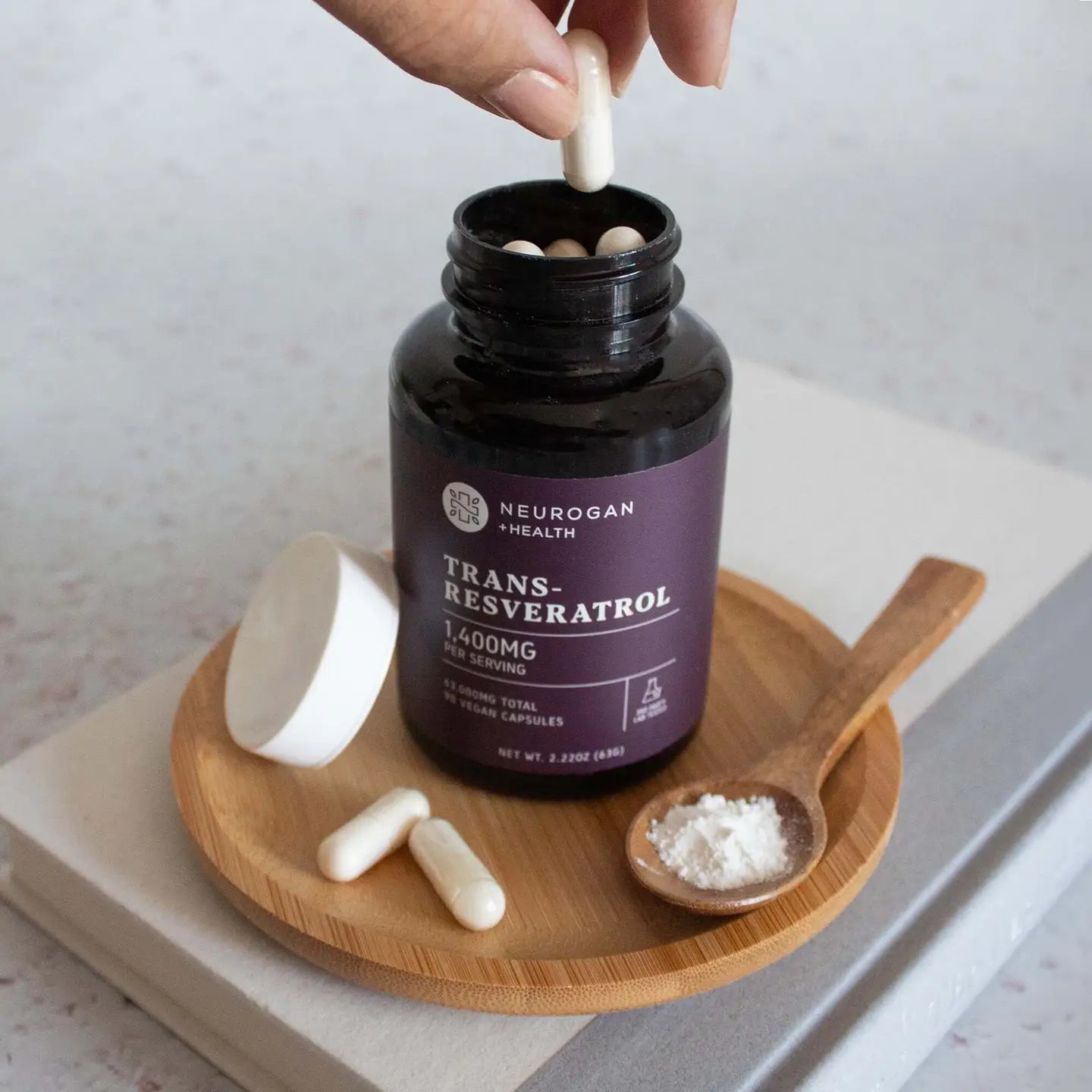 Neurogan Health Trans-Resveratrol supplement bottle with a hand adding a pill, on a wooden tray.