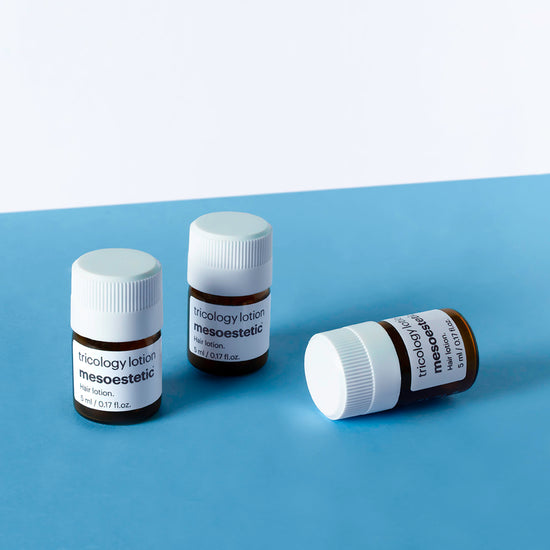 Three bottles of mesoestetic tricology lotion on a blue surface with a white background