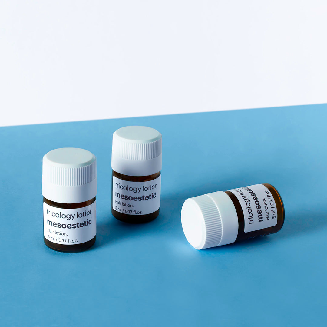 Three bottles of mesoestetic tricology lotion on a blue surface with a white background